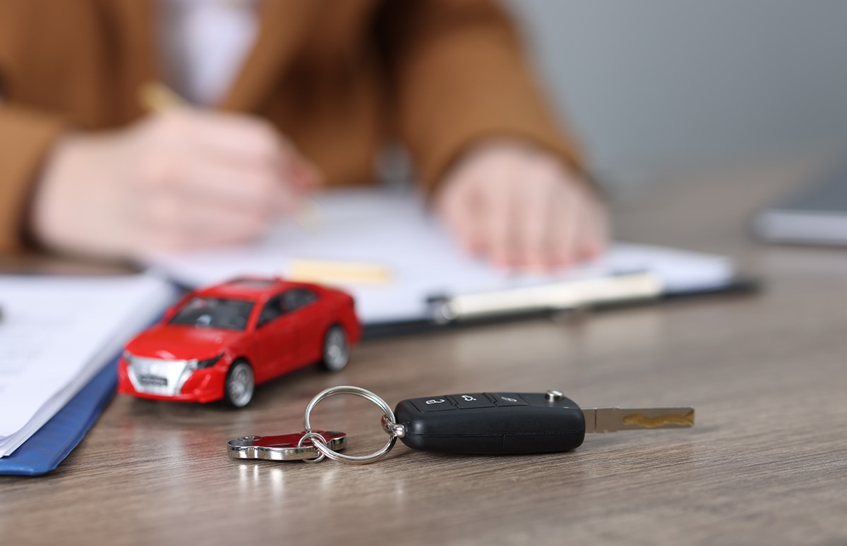 Llaves de coche y coche de juguete sobre una mesa y una mujer firmando doumentación