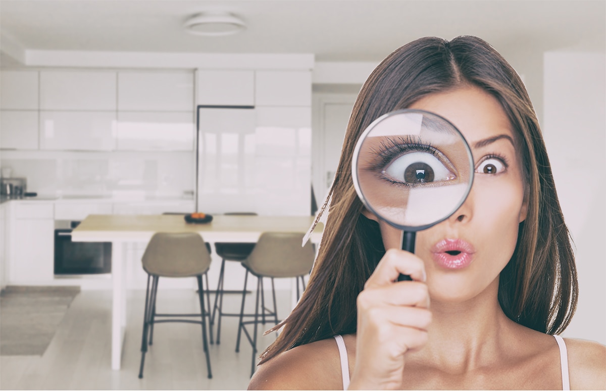 Interior de una vivienda moderna con cocina abierta y comedor, con una persona en primer plano sosteniendo un objeto cerca del pecho y mobiliario doméstico al fondo