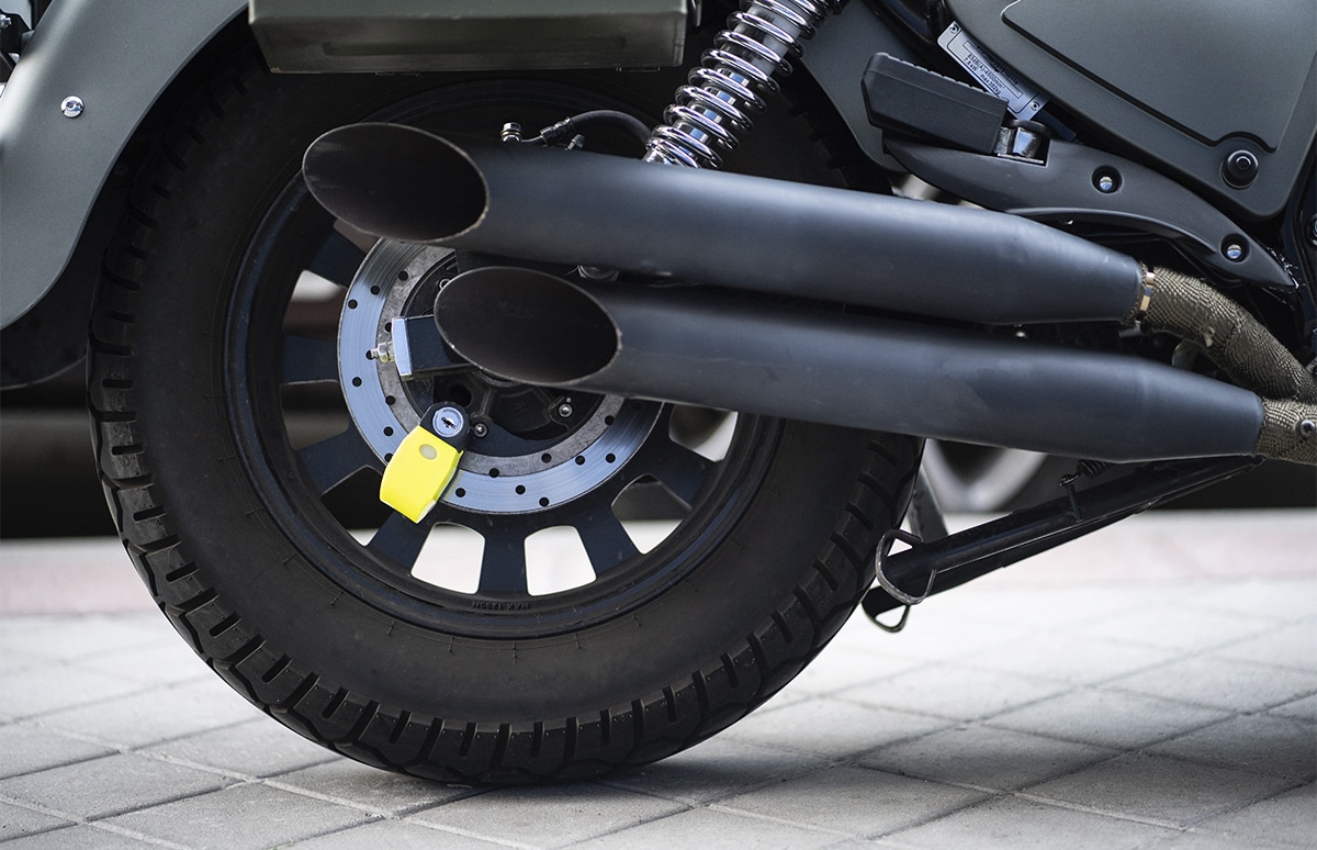 Detalle de la rueda trasera de una motocicleta con sistema antirrobo instalado en el disco de freno, junto al escape y la suspensión