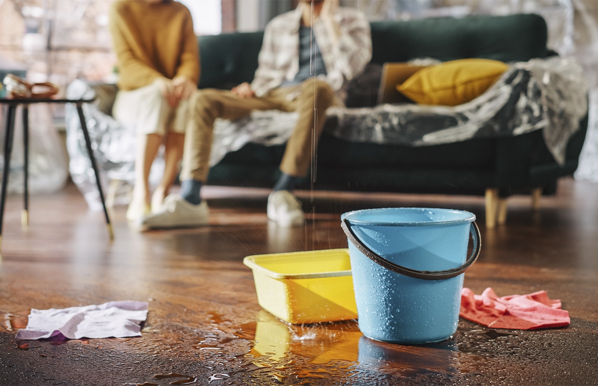 Pareja sentada en un sofá mientras cae agua de una gotera a unos cubos