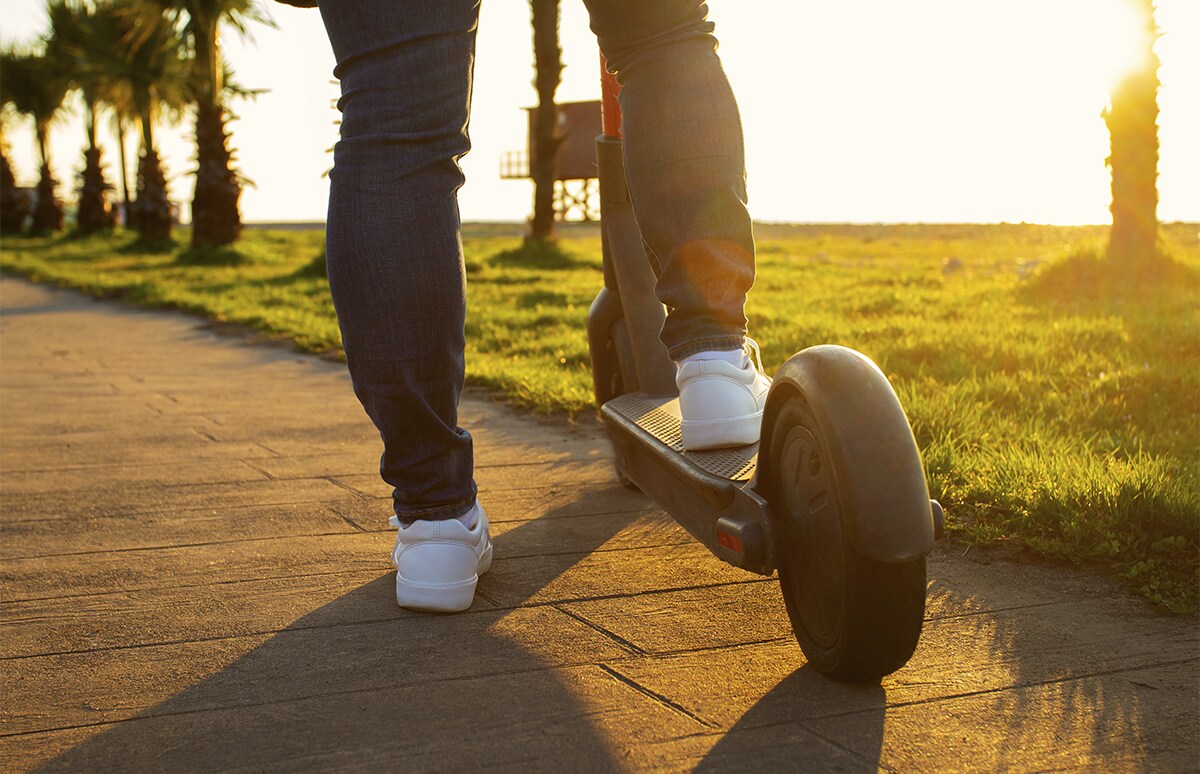 Joven en un paseo con un pie sobre su patinete eléctrico
