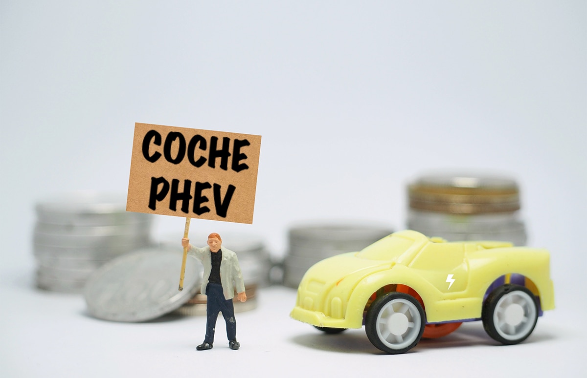 Muñeco con un cartel de Coche PHEV junto a maqueta de coche y monedas al fondo