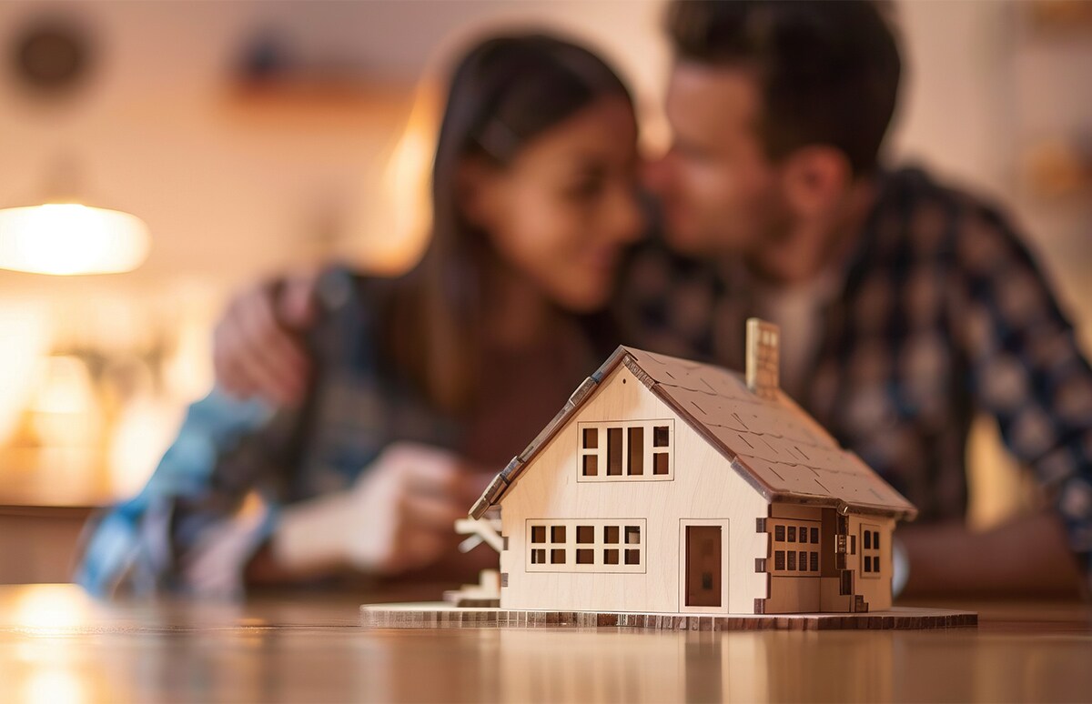 Pareja unida tras una maqueta de madera de una vivienda