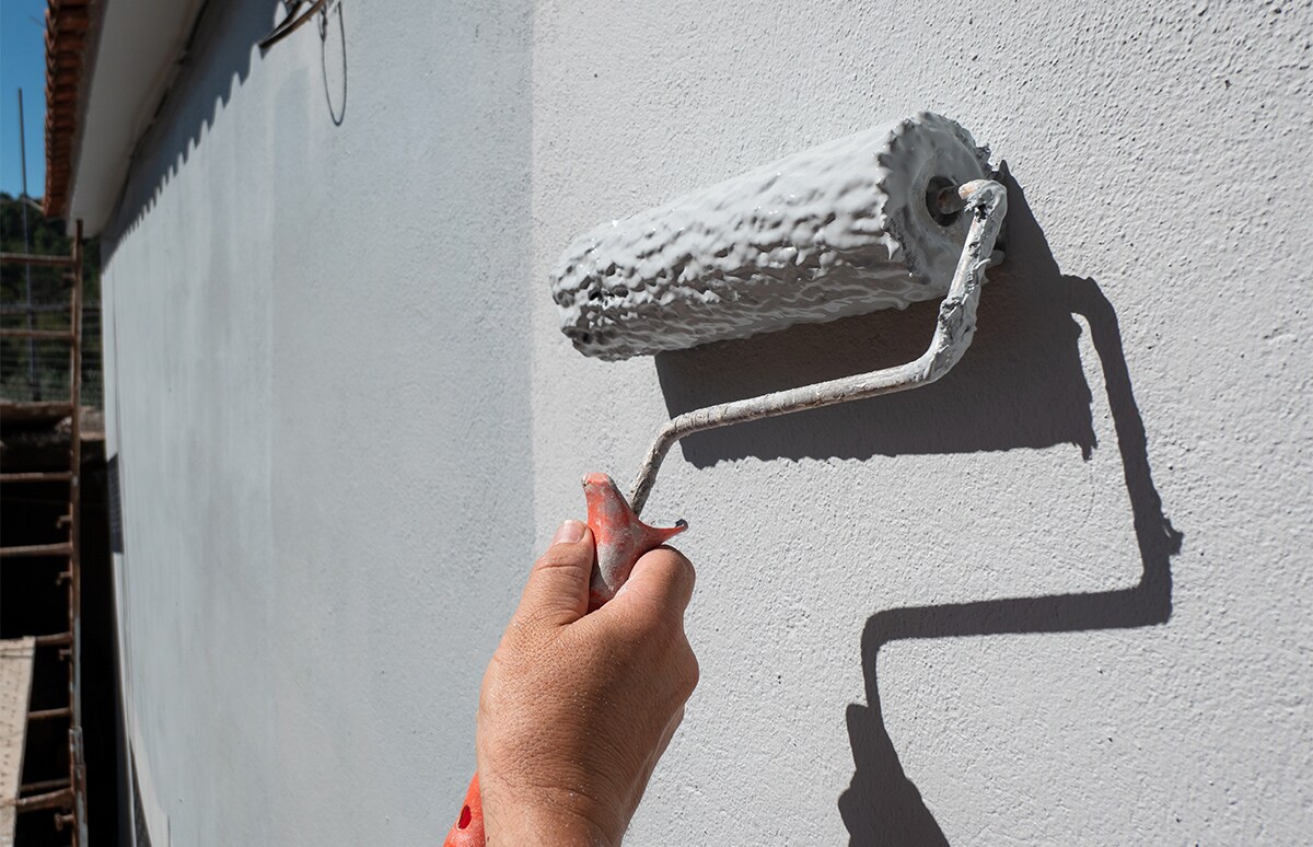 Mano con rodillo de pintar, pintando una pared de blanco