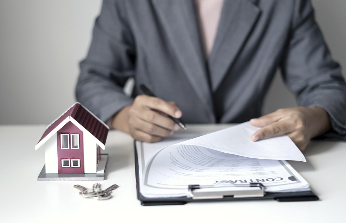 Hombre firmando un contrato de arrendamiento junto a la maqueta de una vivienda y las llaves de la misma