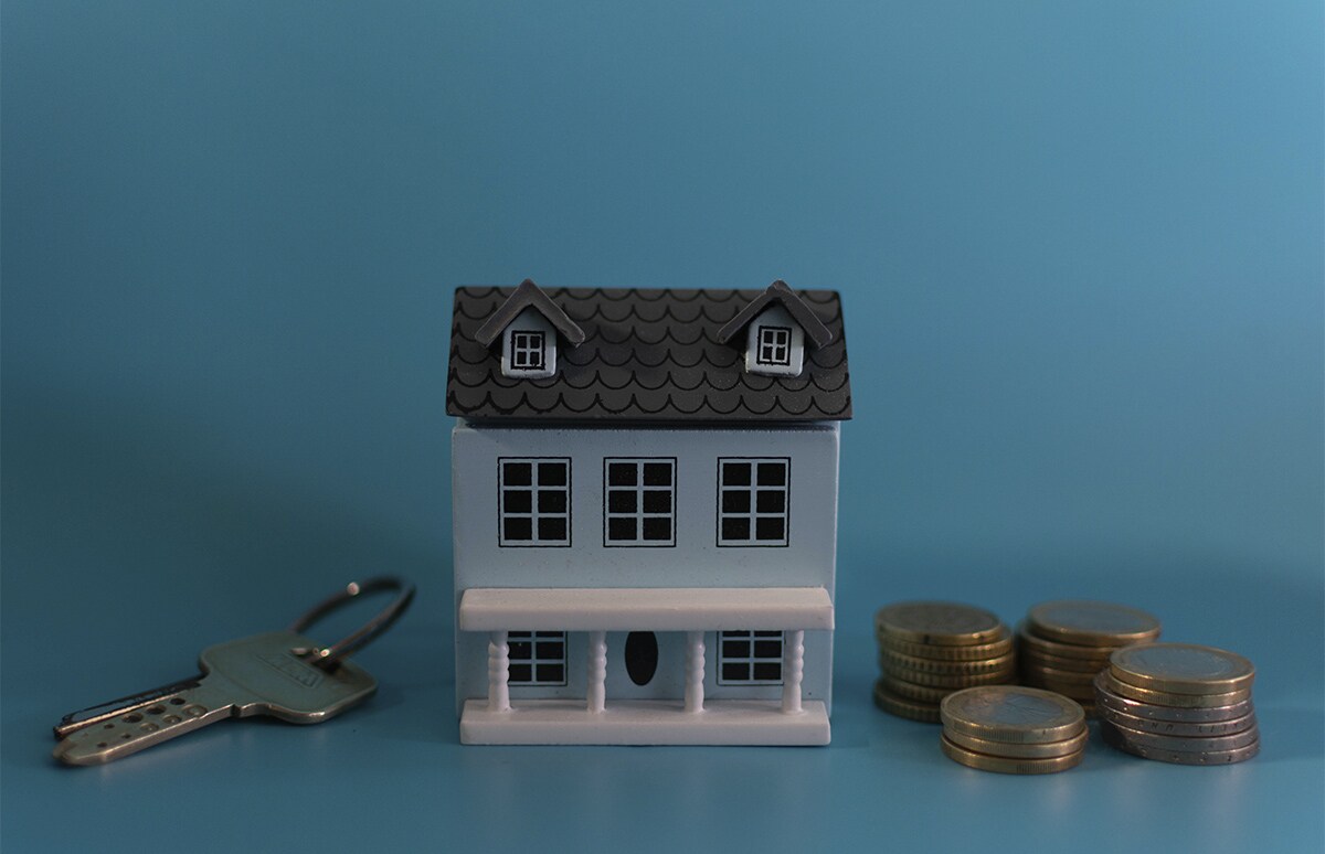 Maqueta de una vivienda con las llaves a un lado y monedas al otro