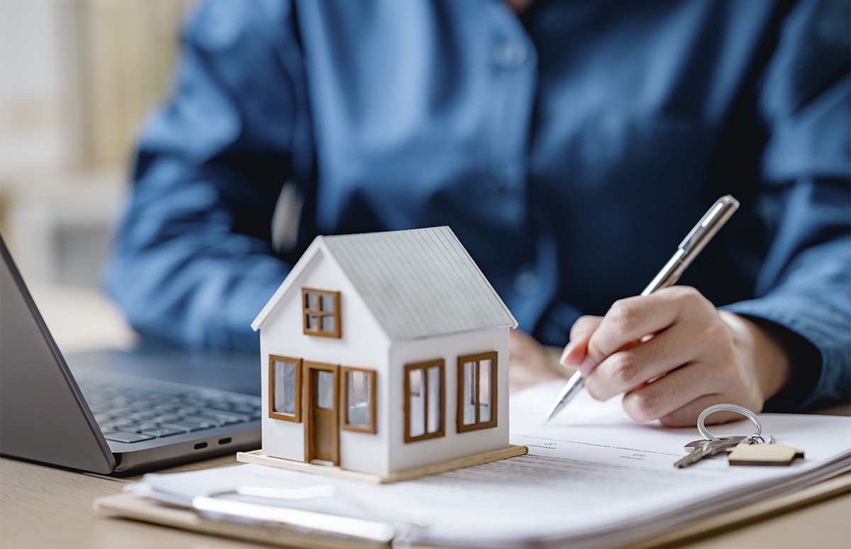 Joven firmando un contrato de hipoteca junto una casa en miniatura y unas llaves