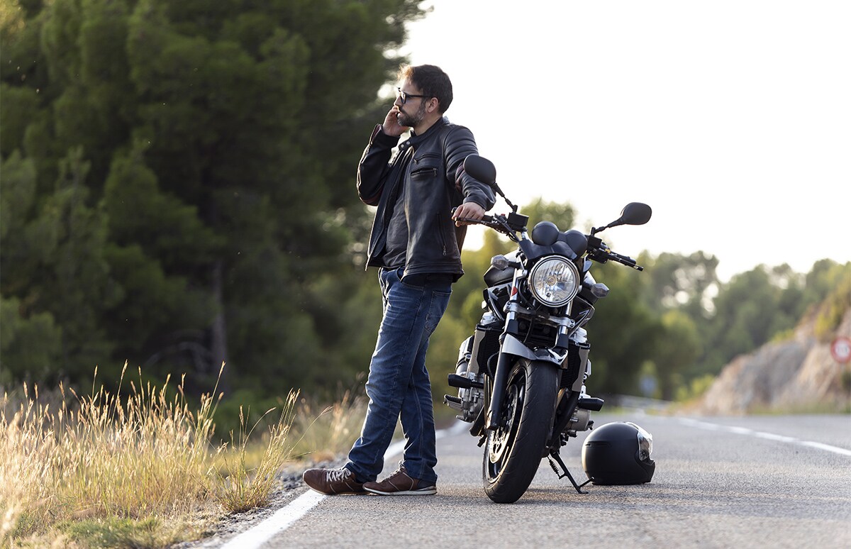 Motorista llamando por teléfono apoyado en su moto y con el casco en el suelo