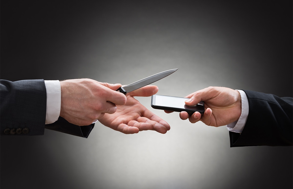 Mano de hombre con cuchillo amenaza y quita el móvil a otra mano que se lo entrega