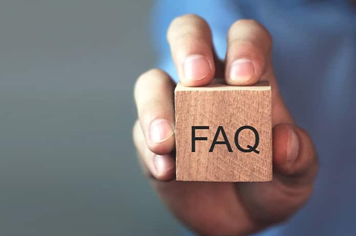 Primer plano de una mano sosteniendo un cubo de madera con la palabra “FAQ” grabada en él