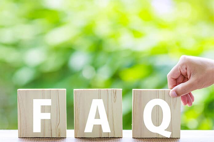 Cubo de madera con las letras “FAQ” en primer plano, sostenido por una mano sobre un fondo natural desenfocado