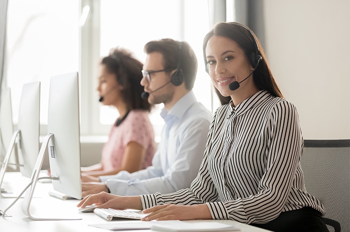 Equipo de atención al cliente trabajando en una oficina luminosa, con varias personas utilizando auriculares frente a ordenadores en puestos alineados