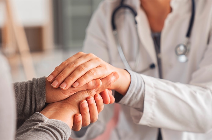 Manos de un profesional sanitario ofreciendo apoyo al colocar sus manos sobre las de otra persona