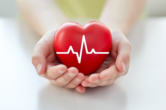 Manos sosteniendo una figura de corazón rojo con un diseño de línea de electrocardiograma en la superficie