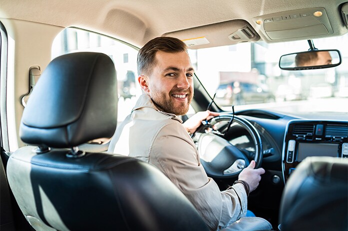 Interior de un vehículo urbano, con una persona al volante en un entorno de tráfico y edificios al fondo
