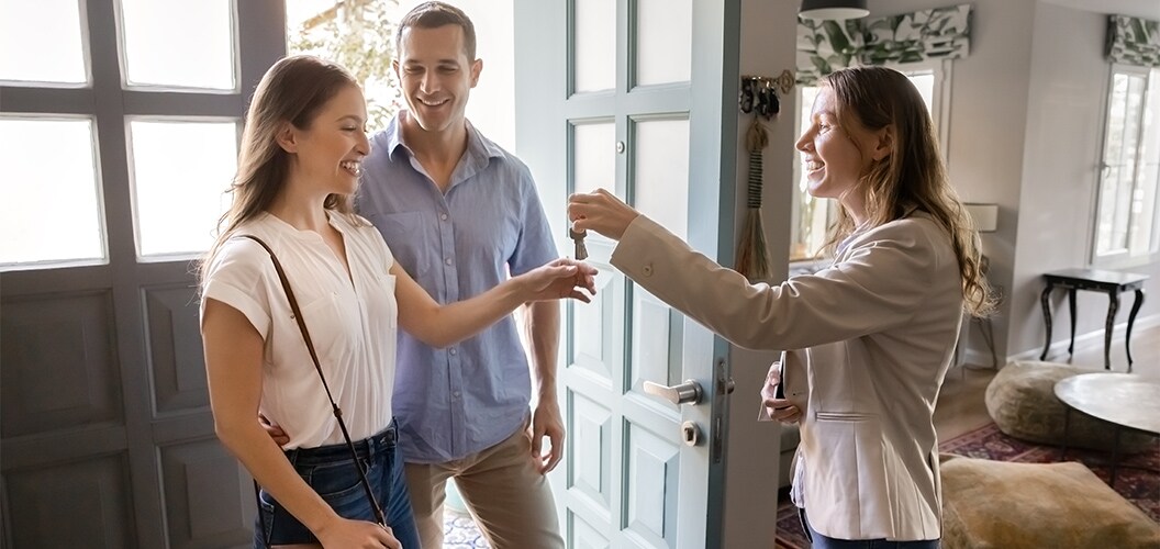 Entrega de llaves en la entrada de una vivienda, con varias personas de pie junto a la puerta en un entorno doméstico luminoso