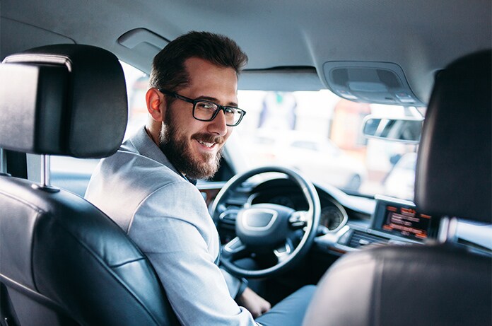 Interior de un automóvil visto desde la parte trasera, con el conductor girando ligeramente mientras el volante y el panel de control quedan en primer plano