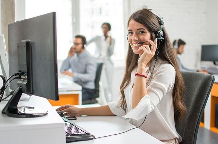 Persona utilizando auriculares y un ordenador de sobremesa en un entorno de oficina, con otros puestos de trabajo visibles al fondo