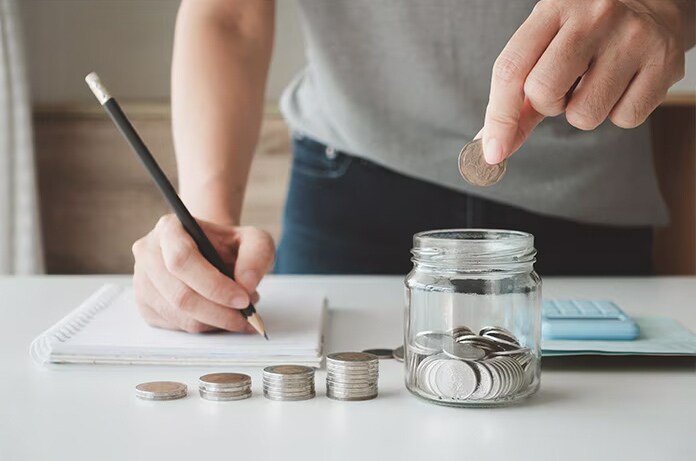 Manos organizando y contando monedas mientras se anotan gastos en una libreta, simbolizando planificación financiera