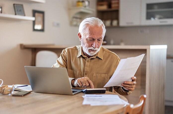 Persona mayor gestionando documentos y usando un ordenador portátil en la mesa de su hogar