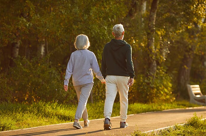 Pareja mayor paseando de la mano por un sendero iluminado por la cálida luz del atardecer