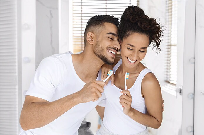 Dos personas frente al espejo cepillándose los dientes juntas en un baño iluminado