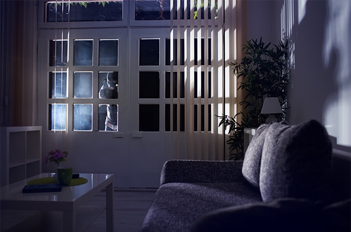 Figura encapuchada intentando acceder al interior de una vivienda a través de una puerta acristalada por la noche