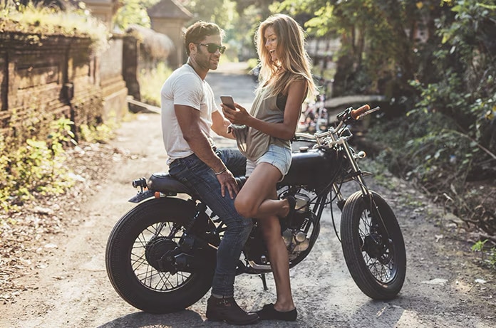 Dos personas conversando junto a una motocicleta en un camino rodeado de vegetación