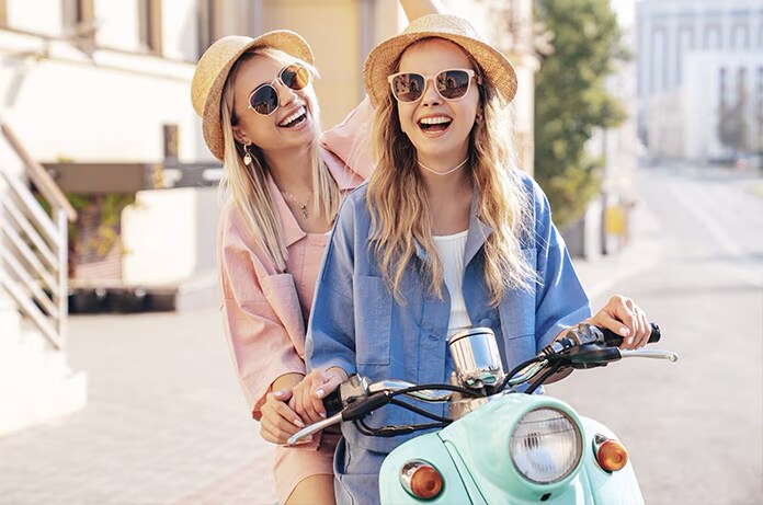 Dos personas compartiendo un paseo en un ciclomotor azul claro en una calle luminosa