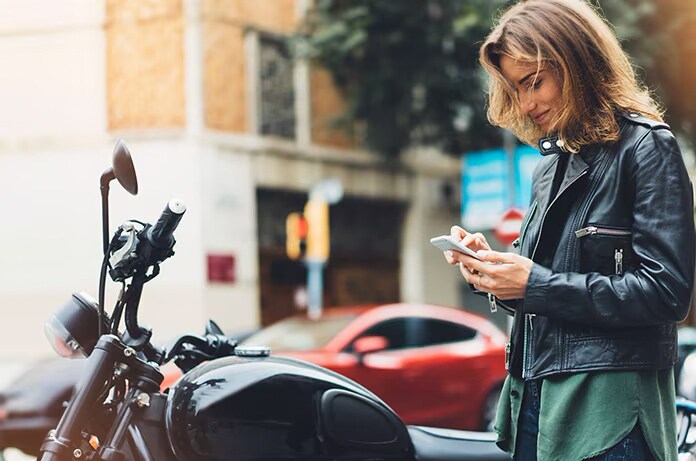 Persona de pie junto a una motocicleta consultando un teléfono en una calle transitada