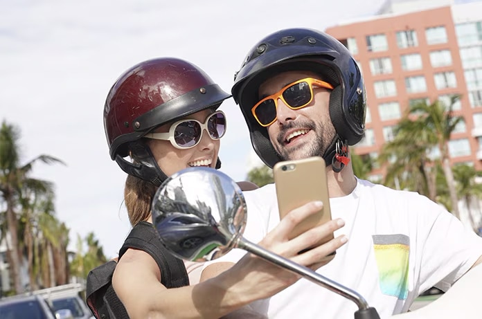 Dos personas haciendo una fotografía con un teléfono mientras permanecen sobre un ciclomotor
