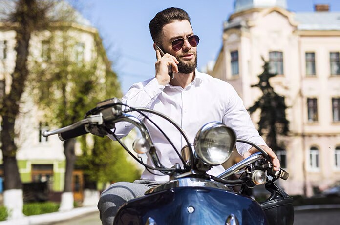 Persona hablando por teléfono mientras esta sentado en una motocicleta en una calle con edificios clásicos