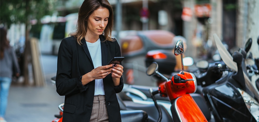 Persona de pie junto a una moto aparcada en una calle urbana mientras utiliza un teléfono móvil