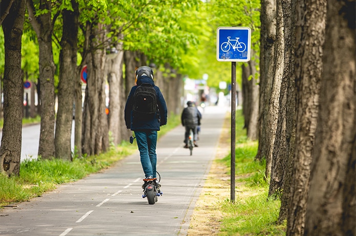 Usuario circulando en patinete eléctrico por un carril bici rodeado de árboles