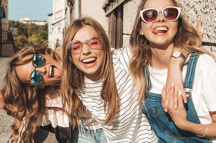 Tres personas caminando juntas en una calle soleada, abrazadas por los hombros y mostrando una actitud dinámica