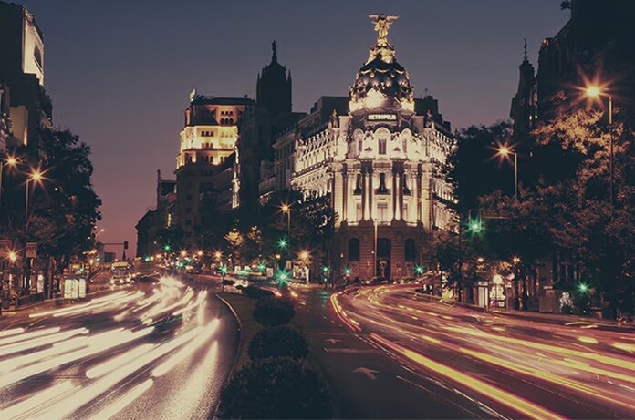 Cruce urbano del Madrid nocturno con el edificio histórico Metrópolis iluminado y estelas de luz creadas por el tráfico