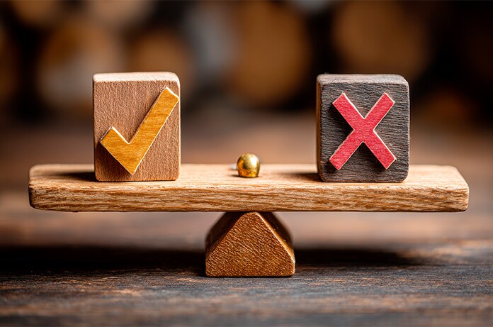 Balanza de madera en equilibrio con dos bloques: uno con un símbolo de verificación en color amarillo y otro con una cruz en rojo, represe