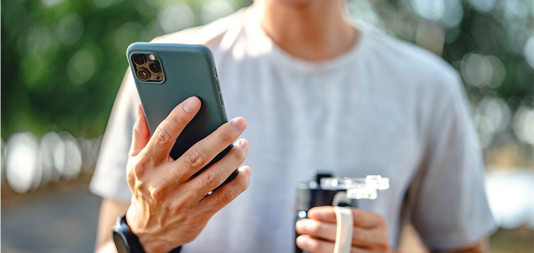 Persona sosteniendo un teléfono móvil en un entorno exterior con fondo desenfocado